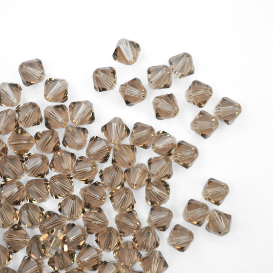 Austrian crystal 5328 bicone beads in the color Greige spilling out onto a white background. 