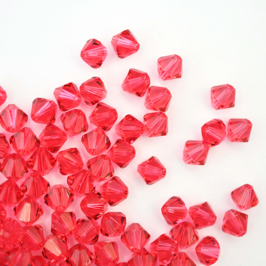 Austrian crystal 5328 bicone beads in the color Indian Pink spilling out onto a white background. 