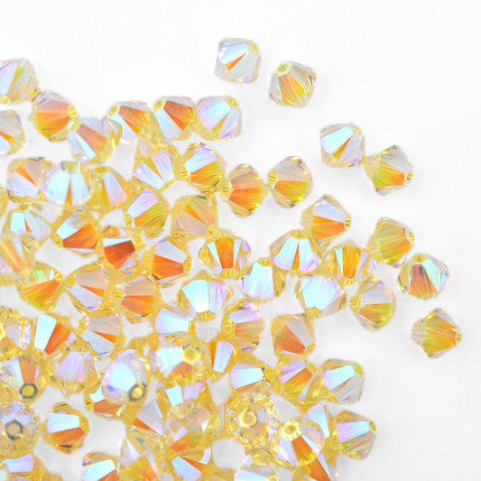 Austrian crystal 5328 bicone beads in the color Jonquil AB 2X spilling out onto a white background. 
