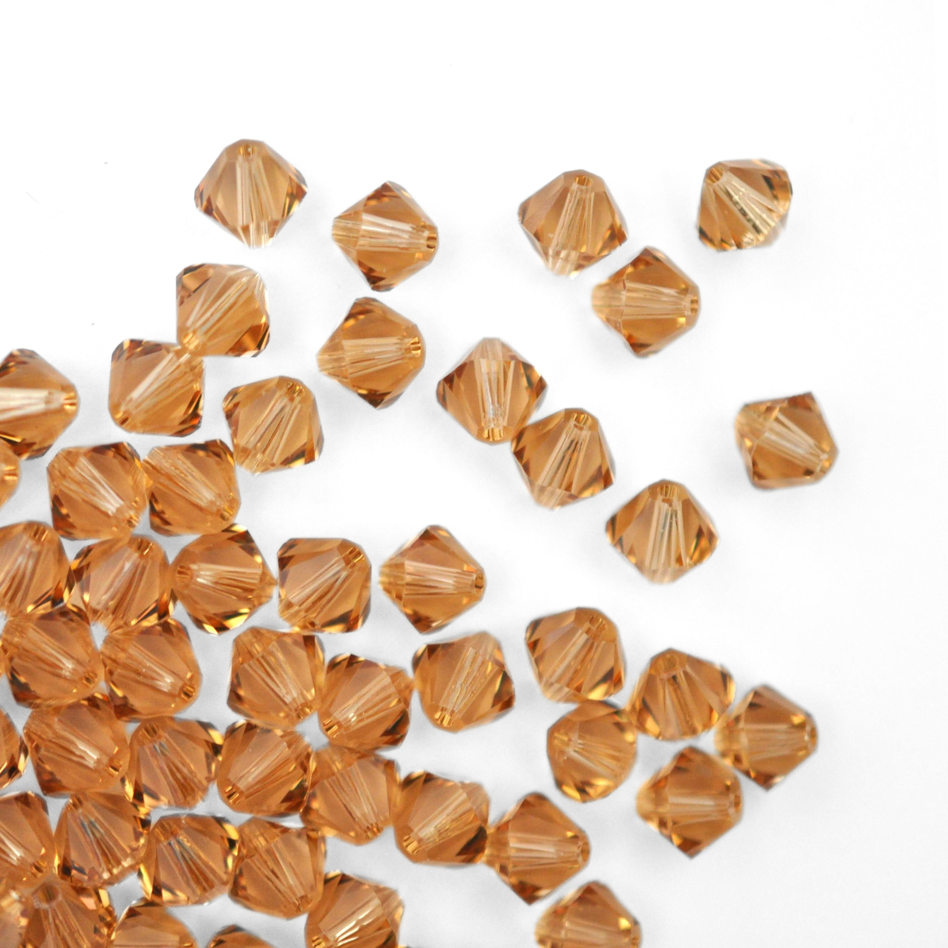 Austrian crystal 5328 bicone beads in the color Light Colorado Topaz spilling out onto a white background. 