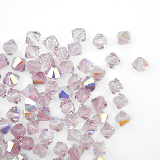 Austrian crystal 5328 bicone beads in the color Light Amethyst AB spilling out onto a white background. 