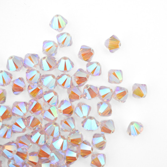 Austrian crystal 5328 bicone beads in the color Light Amethyst AB 2X spilling out onto a white background. 