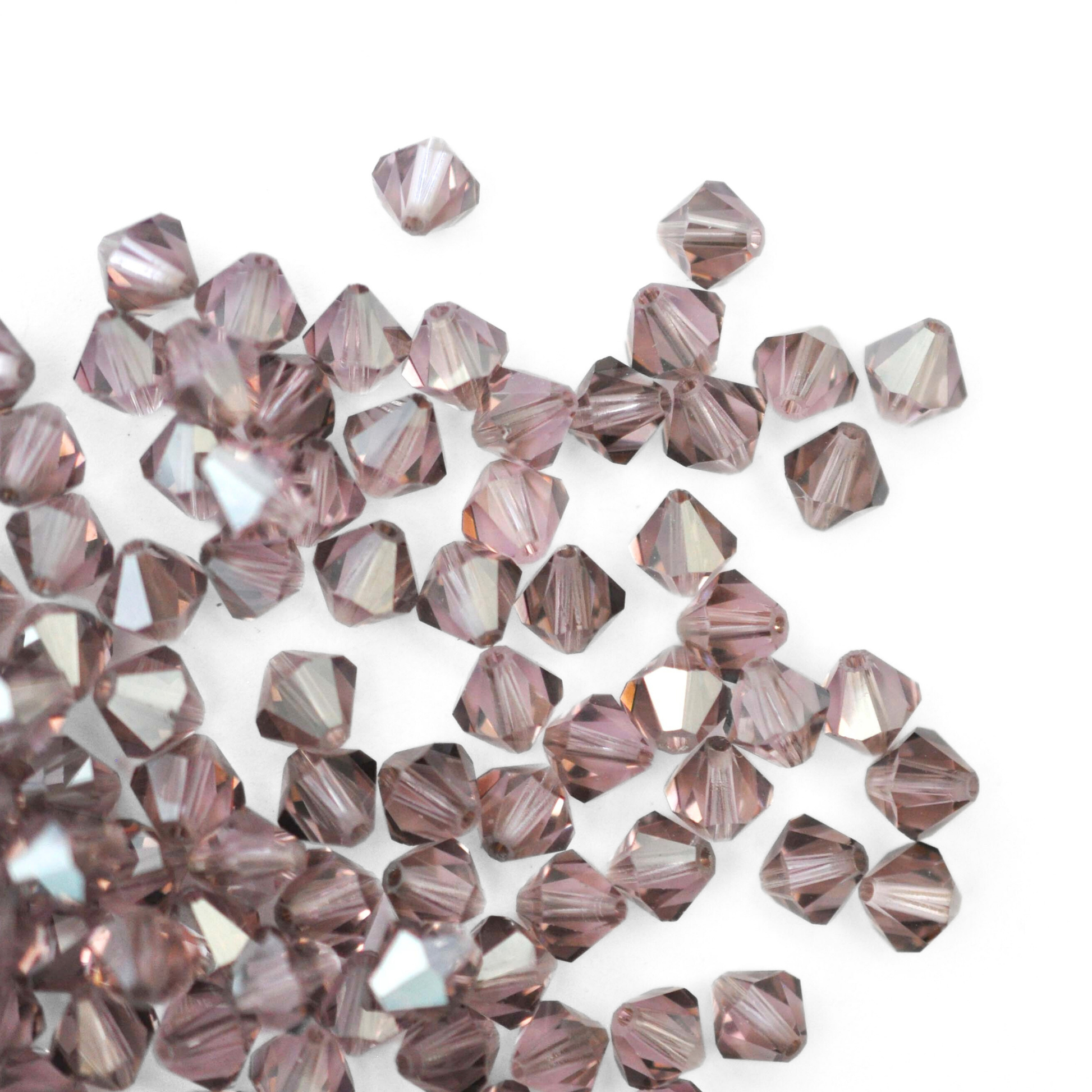 Austrian crystal 5328 bicone beads in the color Light Amethyst Satin spilling out onto a white background. 
