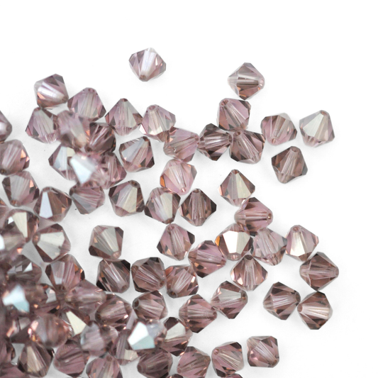 Austrian crystal 5328 bicone beads in the color Light Amethyst Satin spilling out onto a white background. 