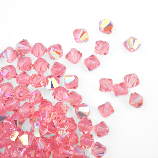 Austrian crystal 5328 bicone beads in the color Light Rose AB spilling out onto a white background. 