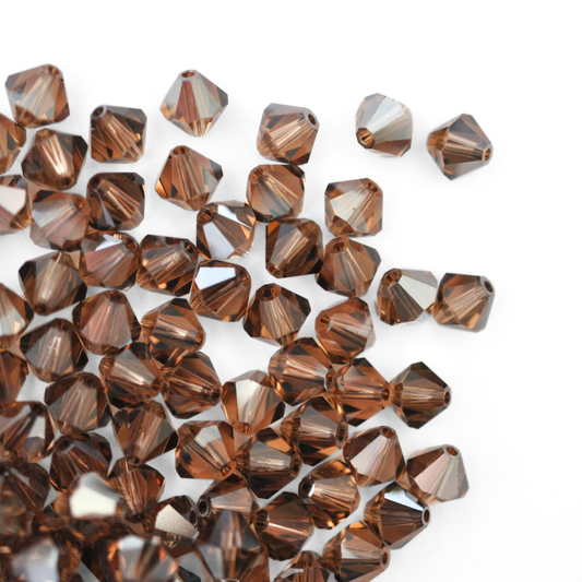 Austrian crystal 5328 bicone beads in the color Light Smoked Topaz Satin spilling out onto a white background. 