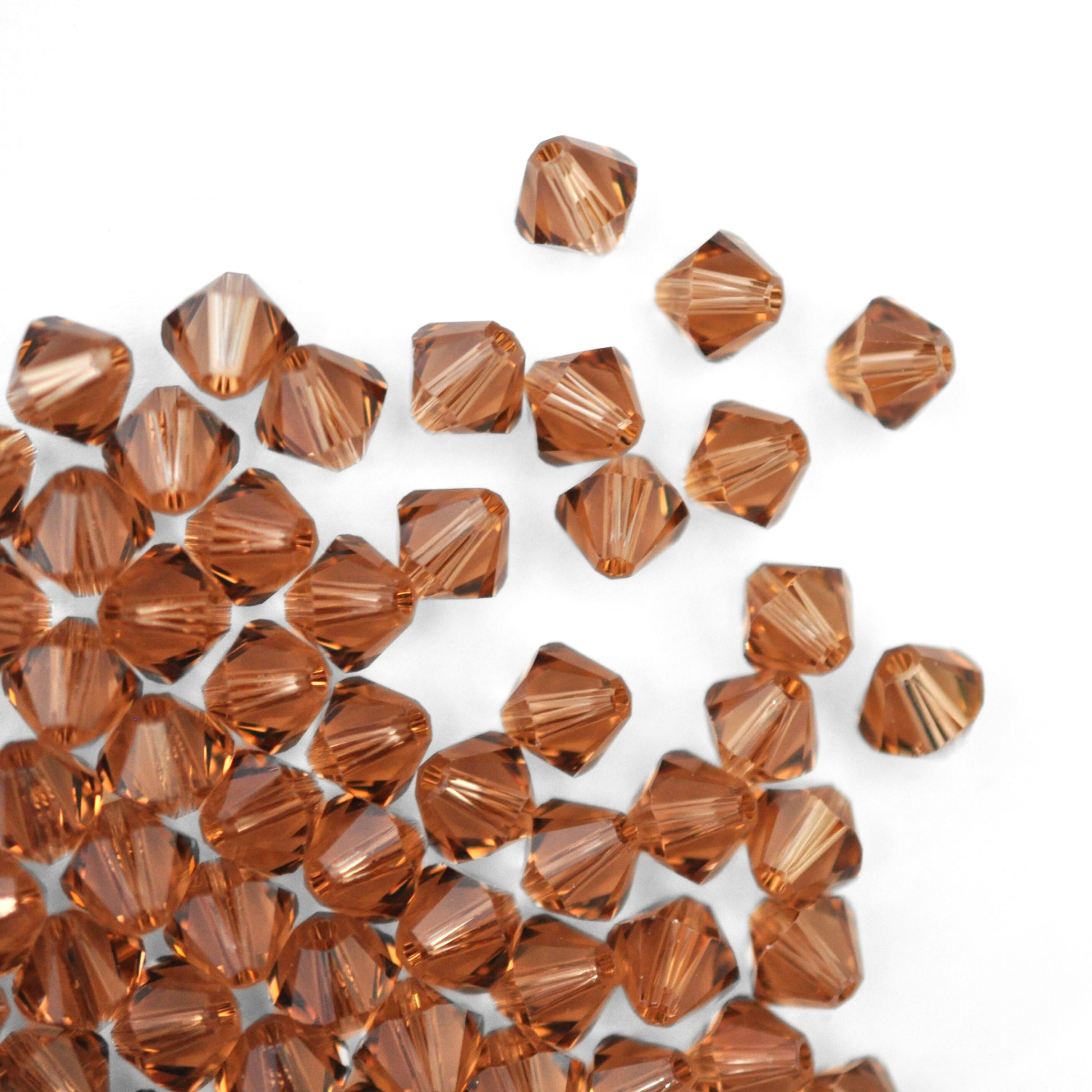 Austrian crystal 5328 bicone beads in the color Light Smoked Topaz spilling out onto a white background. 