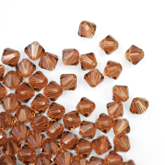 Austrian crystal 5328 bicone beads in the color Light Smoked Topaz spilling out onto a white background. 