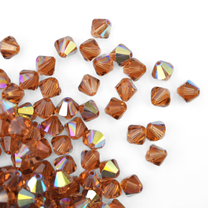 Austrian crystal 5328 bicone beads in the color Light Smoked Topaz AB spilling out onto a white background. 