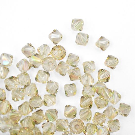 Austrian crystal 5328 bicone beads in the color Luminous Green spilling out onto a white background. 