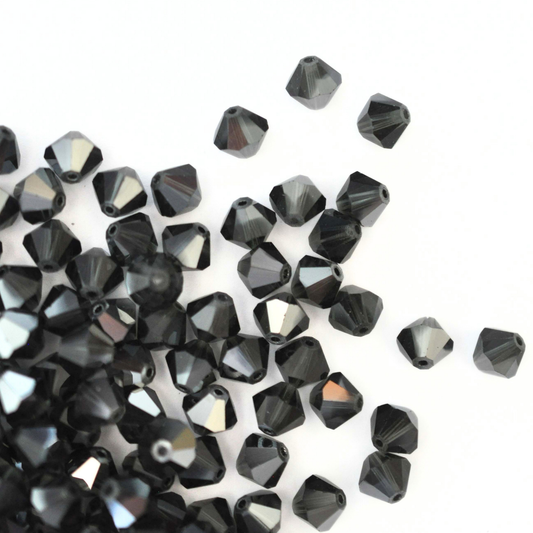 Austrian crystal 5328 bicone beads in the color Morion Satin spilling out onto a white background. 