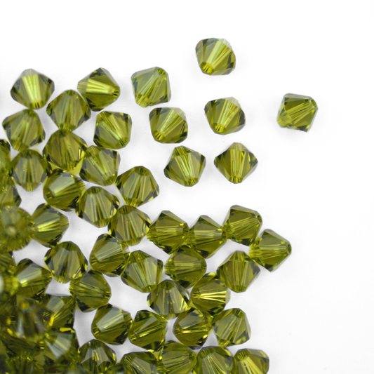 Austrian crystal 5328 bicone beads in the color Olivine spilling out onto a white background. 