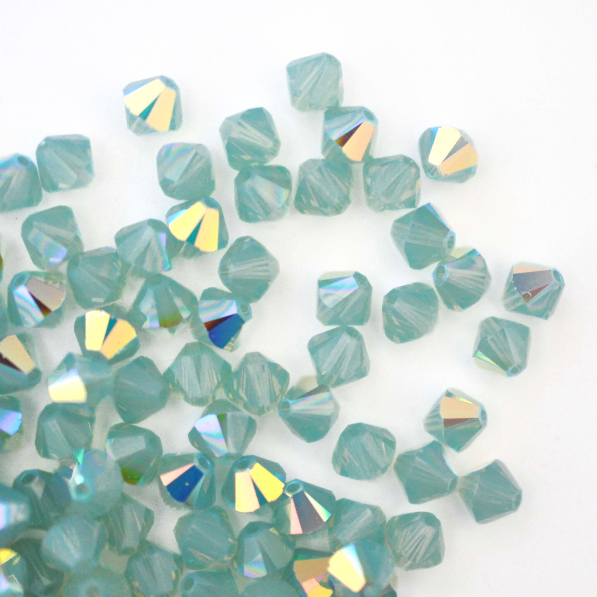 Austrian crystal 5328 bicone beads in the color Pacific Opal AB spilling out onto a white background. 