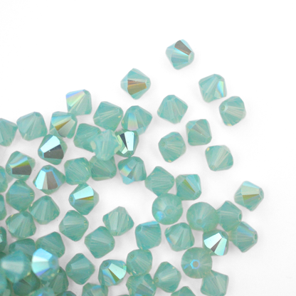 Austrian crystal 5328 bicone beads in the color Pacific Opal Shimmer spilling out onto a white background. 