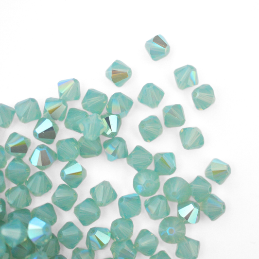 Austrian crystal 5328 bicone beads in the color Pacific Opal Shimmer spilling out onto a white background. 