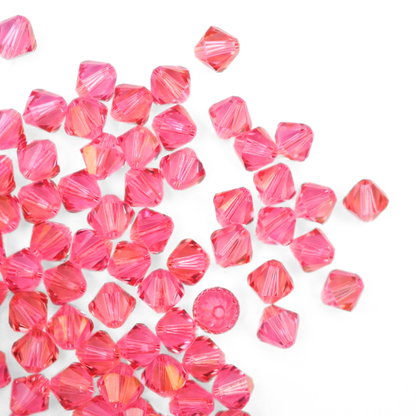 Austrian crystal 5328 bicone beads in the color Rose Champagne spilling out onto a white background. 