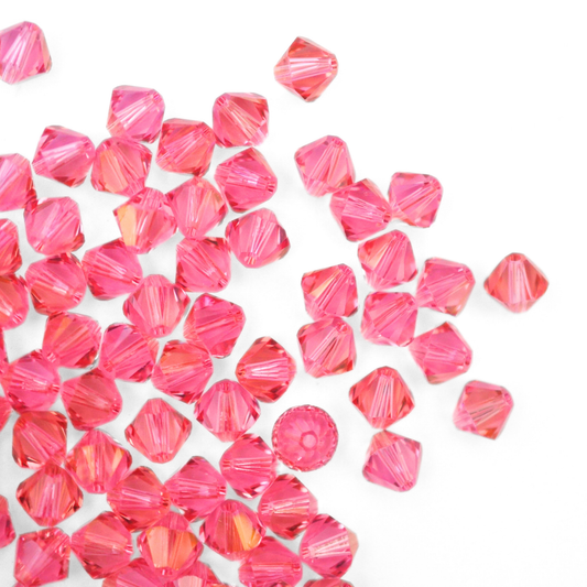 Austrian crystal 5328 bicone beads in the color Rose Champagne spilling out onto a white background. 