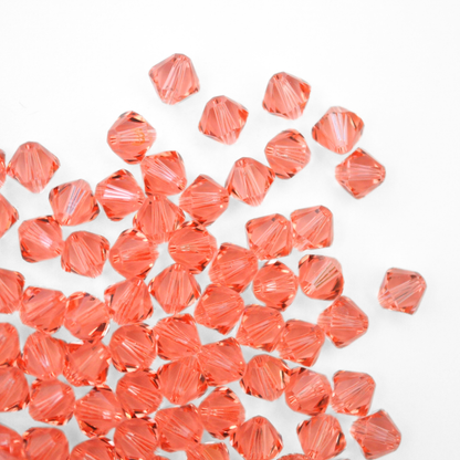 Austrian crystal 5328 bicone beads in the color Rose Peach spilling out onto a white background. 