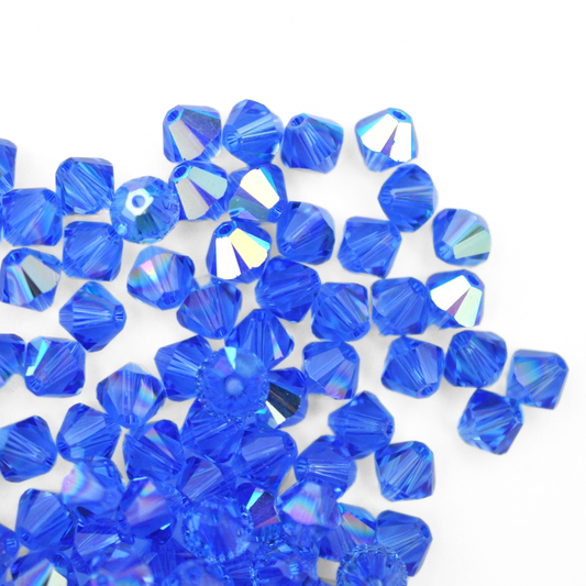 Austrian crystal 5328 bicone beads in the color Sapphire AB spilling out onto a white background. 