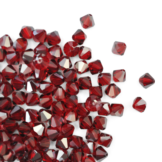 Austrian crystal 5328 bicone beads in the color Siam Satin spilling out onto a white background. 