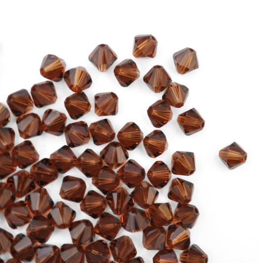 Austrian crystal 5328 bicone beads in the color Smoked Topaz spilling out onto a white background. 