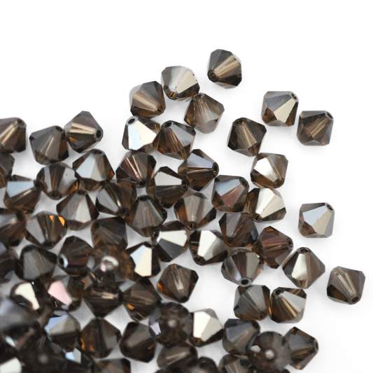 Austrian crystal 5328 bicone beads in the color Smoky Quartz Satin spilling out onto a white background. 