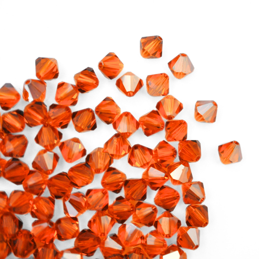 Austrian crystal 5328 bicone beads in the color Sun Satin spilling out onto a white background. 