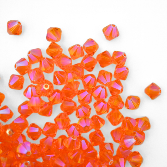 Austrian crystal 5328 bicone beads in the color Sun Shimmer 2X spilling out onto a white background. 