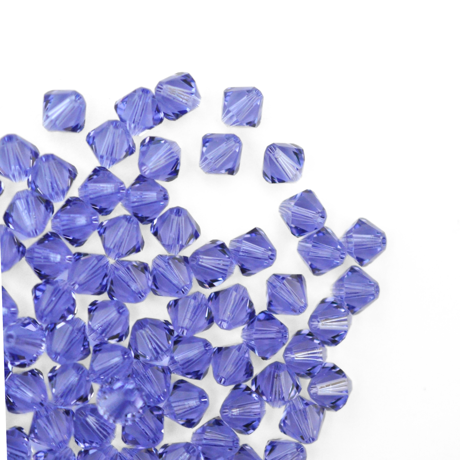 Austrian crystal 5328 bicone beads in the color Tanzanite spilling out onto a white background. 