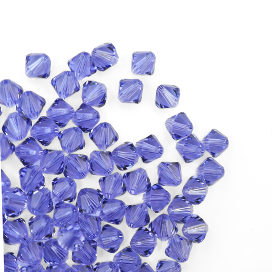 Austrian crystal 5328 bicone beads in the color Tanzanite spilling out onto a white background. 