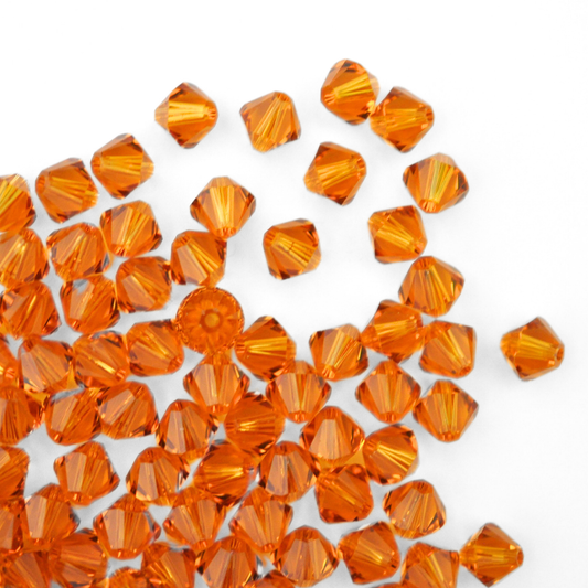 Austrian crystal 5328 bicone beads in the color Topaz spilling out onto a white background. 