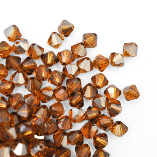 Austrian crystal 5328 bicone beads in the color Topaz Satin spilling out onto a white background. 