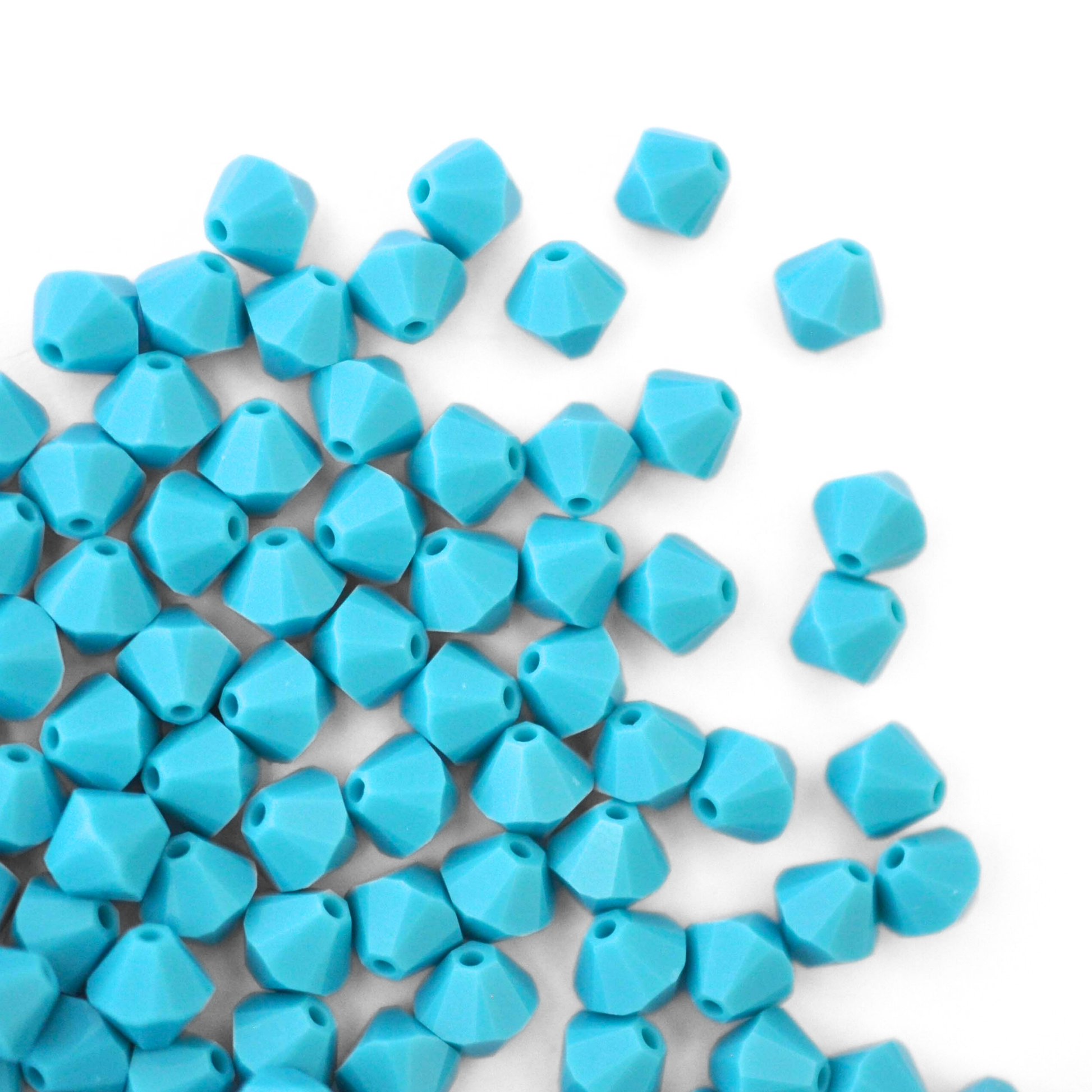 Austrian crystal 5328 bicone beads in the color Turquoise spilling out onto a white background. 
