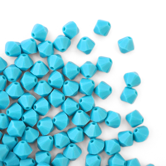 Austrian crystal 5328 bicone beads in the color Turquoise spilling out onto a white background. 