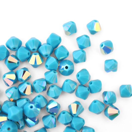 Austrian crystal 5328 bicone beads in the color Turquoise AB spilling out onto a white background. 