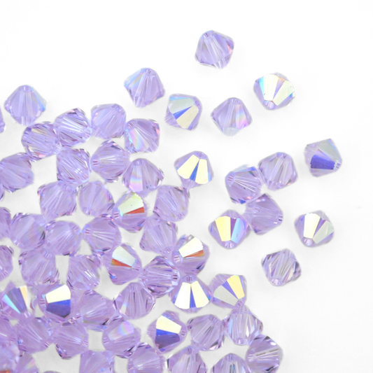 Austrian crystal 5328 bicone beads in the color Violet AB spilling out onto a white background. 