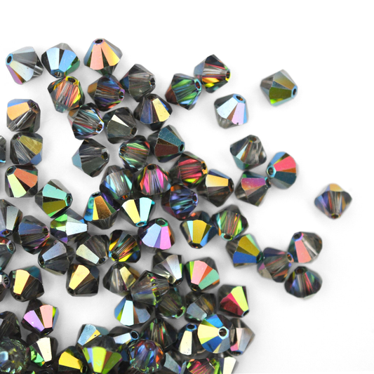 Austrian crystal 5328 bicone beads in the color Vitrail Medium spilling out onto a white background. 