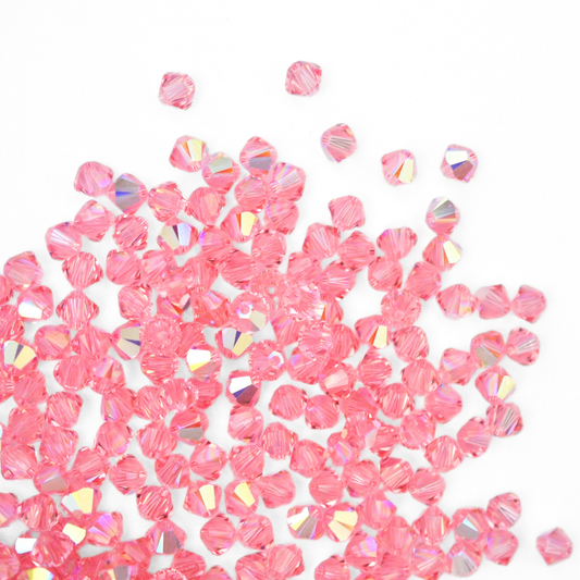 Austrian crystal 5328 bicone beads in the color Light Rose AB spilling out onto a white background. 