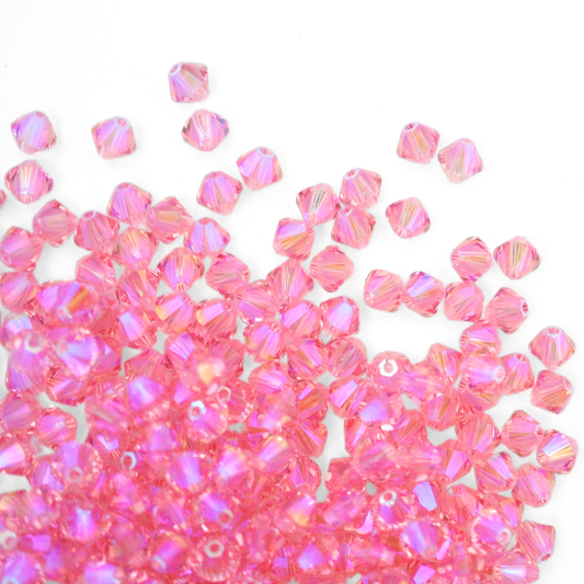 Austrian crystal 5328 bicone beads in the color Light Rose Shimmer 2X spilling out onto a white background. 