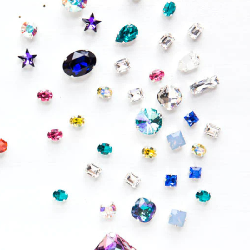A variety of different shaped and sized Austrian Crystals in sew on settings cascading from the top of the images with a white background.